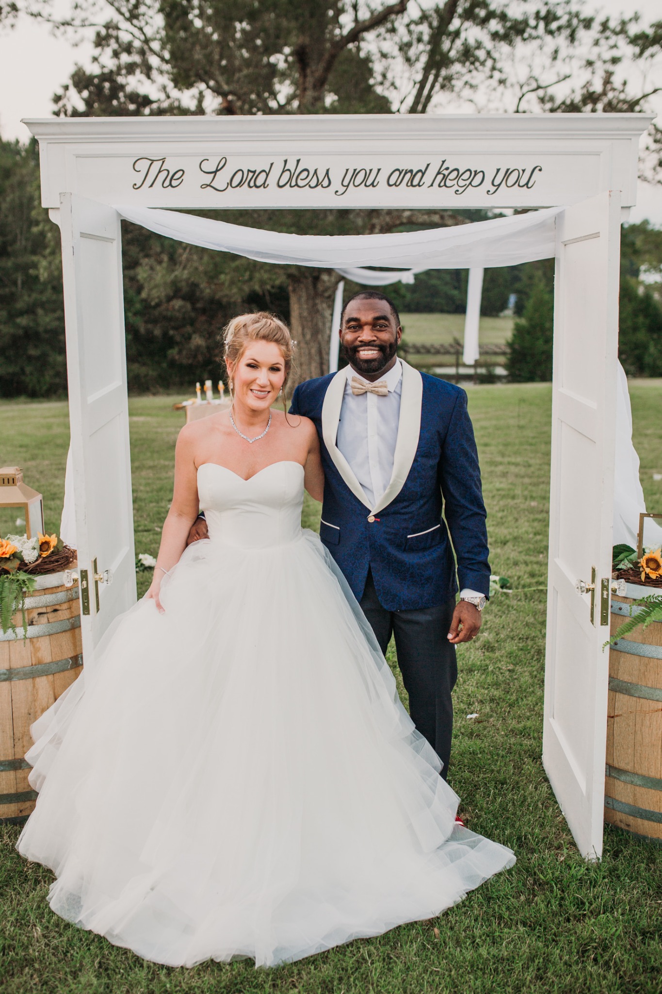 Drew and Sarah on their wedding day, standing together beneath a white outdoor arch