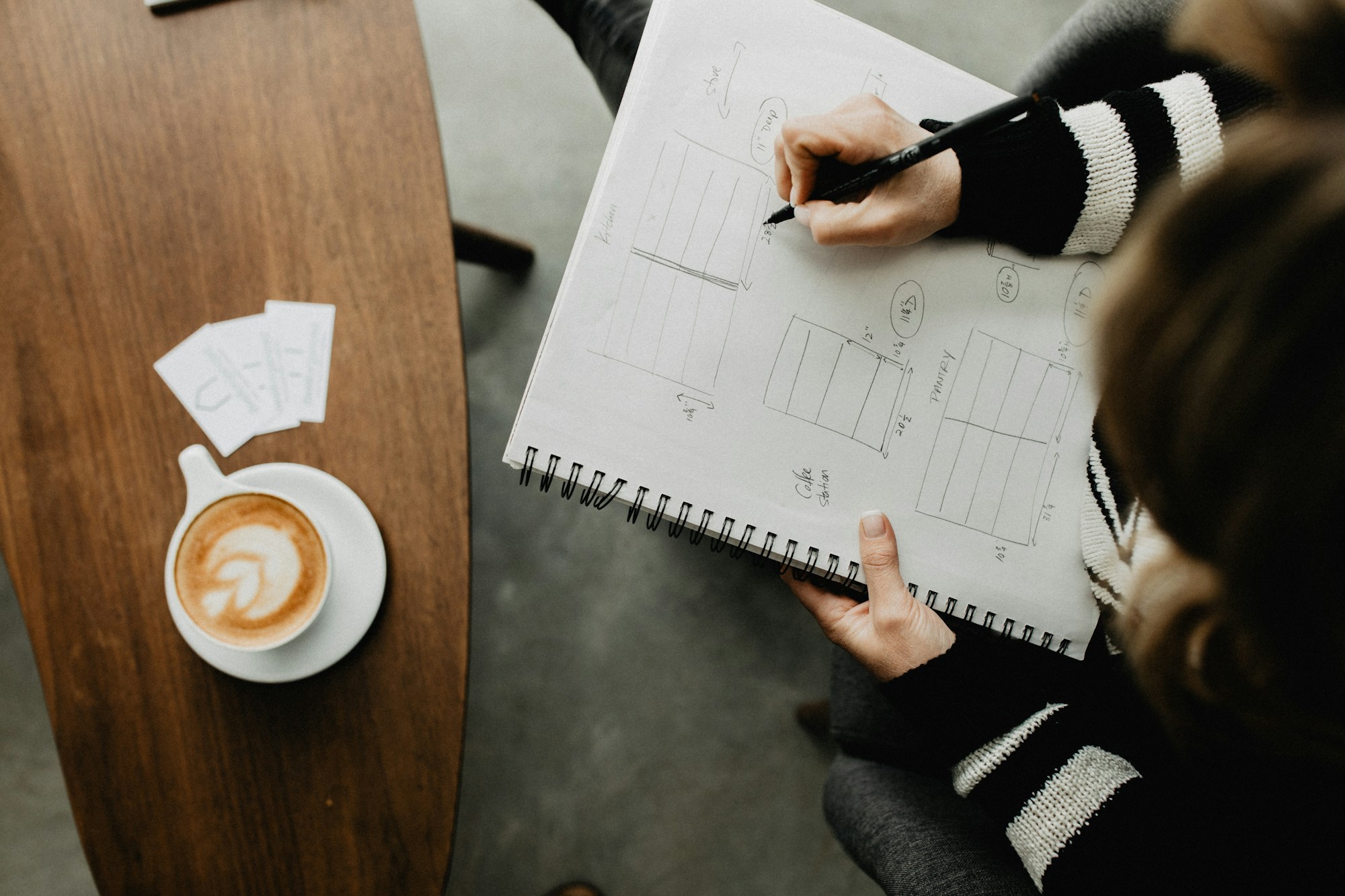 Hands sketching plans in a notebook beside a cup of coffee